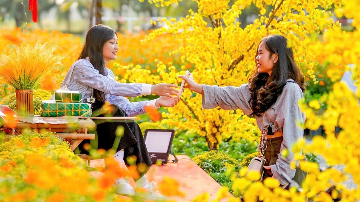 Hai cô gái mặc áo dài chụp ảnh bên tiểu cảnh hoa vàng ngày Tết